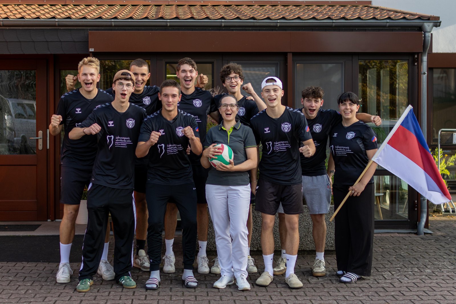 Die Volleyballmannschaft des SV Viktoria Räckelwitz in neuen Shirts, daneben eine Frau mit Ball und eine tschechische Fahne