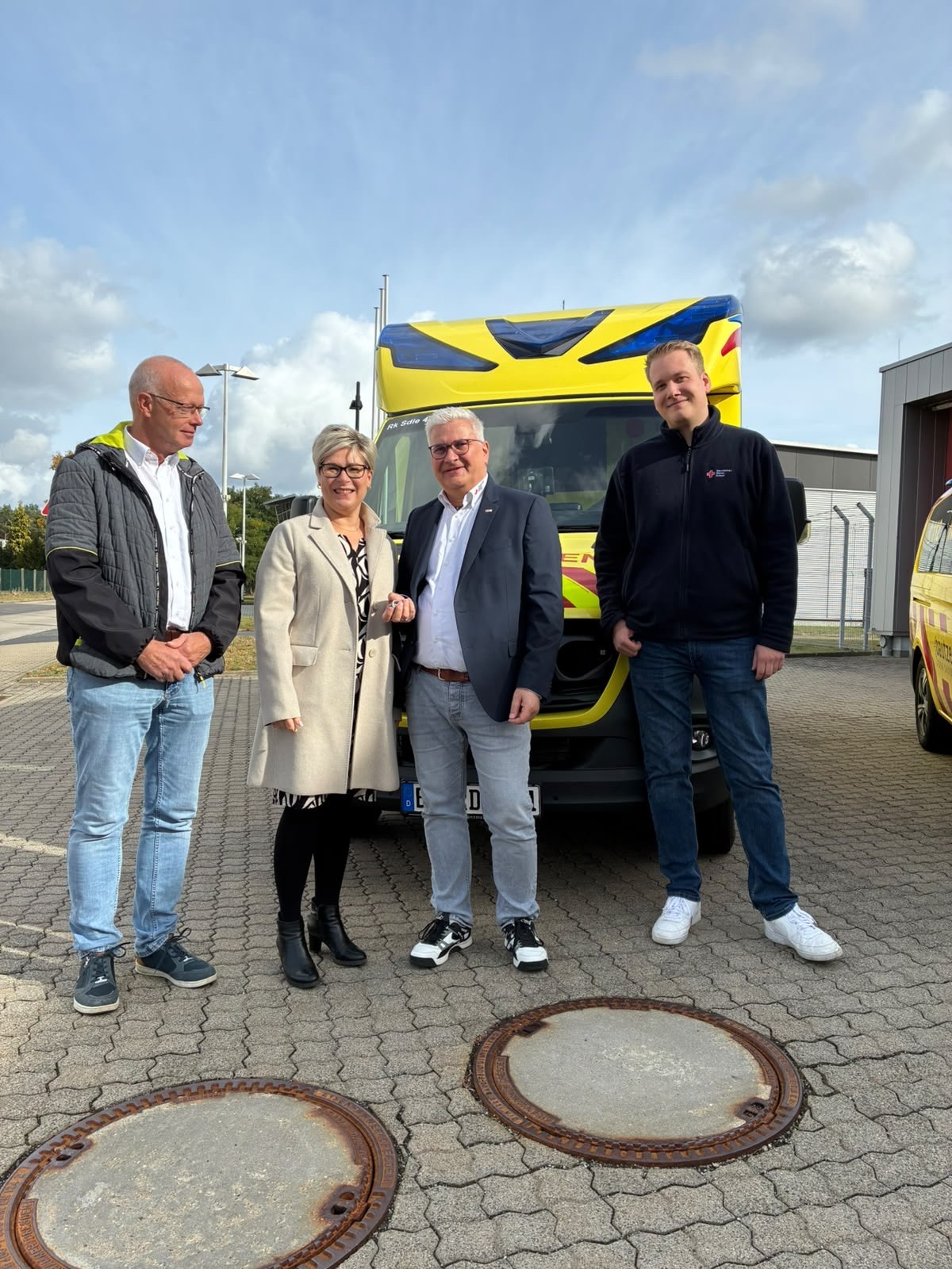 Vier Personen stehen vor einem gelben Rettungswagen, eine Frau hält einen Fahrzeugschlüssel