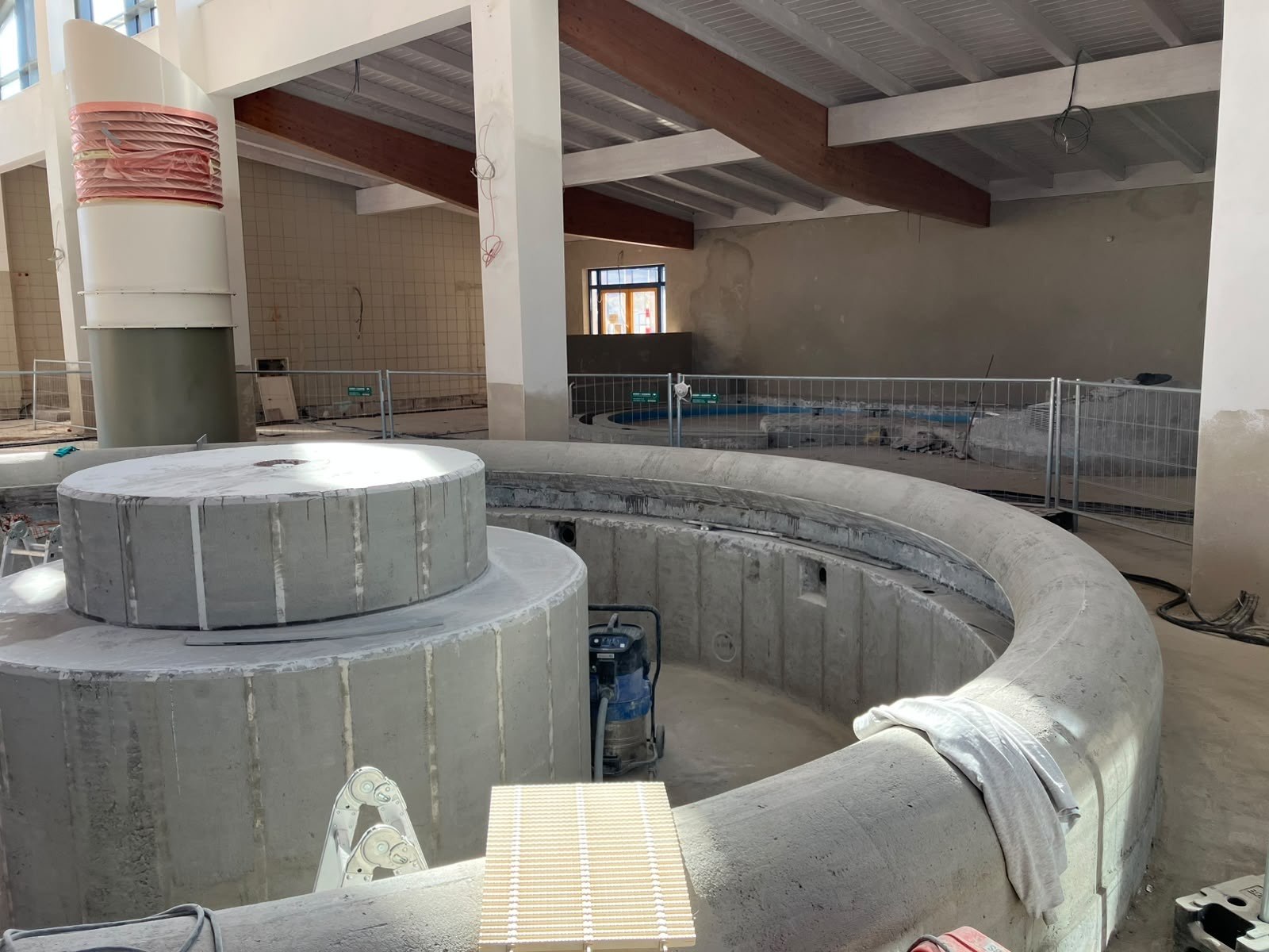 Betonschalen eines runden Beckens in einer Baustellenhalle mit Holzdachstuhl